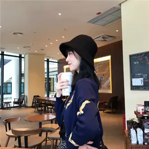 Stijlvolle zwarte wollen vissershoed in gezellige cafésfeer, perfect voor herfst en winter.