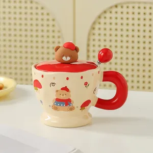 Close-up detail of cute ceramic cartoon bear mug with lid and matching spoon in cream and red.