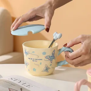 Primo piano di una tazza in ceramica con stampa a farfalla, coperchio e cucchiaio.