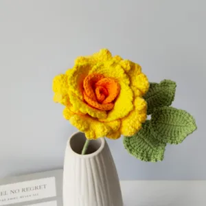 Detailed view of handmade crochet yellow rose flower with green leaves in a white ceramic vase.