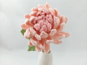 Gros plan détaillé de fleur de dahlia rose dégradé au crochet fait main avec vase en céramique.