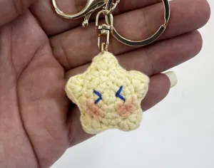 Detalle de llavero de estrella amarilla de ganchillo hecho a mano con cara bordada y anilla.