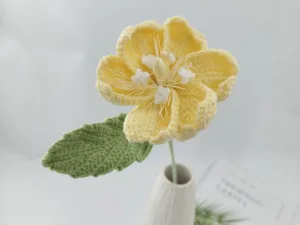 Detailed close-up view of handmade crochet yellow wool flower with green leaf in vase.