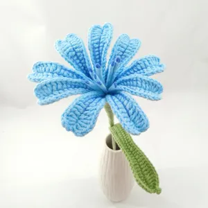 Detailed shot of handmade crochet blue flower with green stem in white ceramic vase decor.