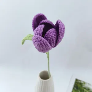 Handgemachte gehäkelte purpurne Tulpenblume mit grünem Stiel in einer eleganten weißen Keramikvase.