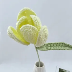 Nahaufnahme eines handgefertigten gelben Häkeltulpenblumendetails mit grünem Blatt und Stil.