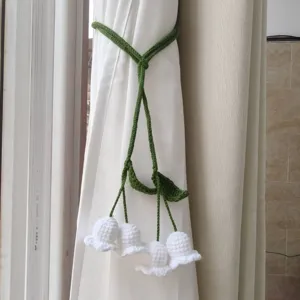Handmade knitted curtain tie-back with white flower bells, creative home decor detail shot.