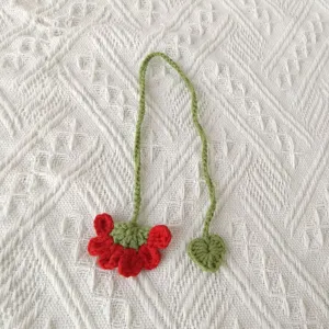 Handmade crochet yarn bookmark detail, cute red flower green leaf design on white fabric background.