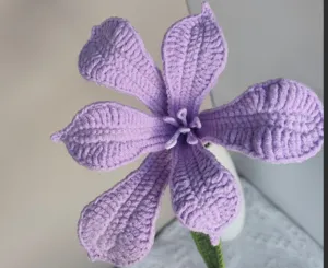 Close-up detail of handmade purple crochet flower petal texture and green stem decor.