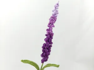 Nahaufnahme einer handgehäkelten Lavendelblüte mit violetten Farbverläufen und grünem Stiel.