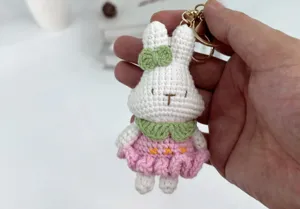 Handgefertigter Häkelhase Schlüsselanhänger mit rosa Kleid und grüner Schleife als Taschendeko.