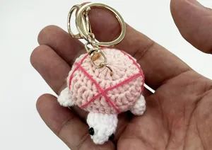 Close-up detail of a handmade crochet turtle keychain with a cute pink shell and gold clasp.