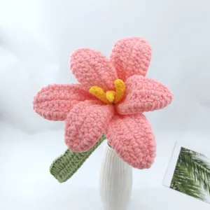Closeup detail of handmade crocheted pink flower with yellow stamen in white vase decor.