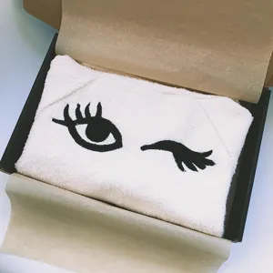 Detailaufnahme eines weissen Haustier-Badetuchs mit besticktem Augen-Design im Geschenkkarton.
