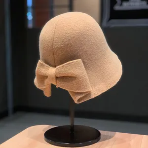 Detailed view of a beige knitted bucket hat with a large bow on the back, soft woolen texture.