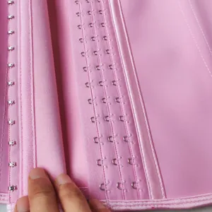 Close-up detail of pink latex waist trainer showing hook and eye closures and fine stitching.