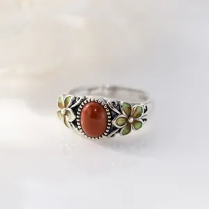 Close-up detail of retro silver ring featuring a red oval stone and green floral accents.