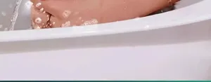 Detail view of pet bathing with splashing water and foam in a clean white bathtub setup.