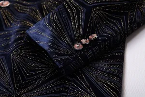 Primer plano de los detalles de chaqueta de terciopelo azul con patron geometrico dorado y botones.