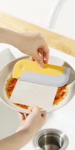Detail view of the yellow and grey kitchen scraper cleaning grease off a ceramic plate.