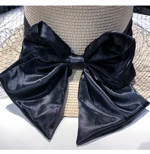 Detailed close-up of a women's black satin bow and mesh veil on a summer straw hat.