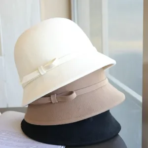 Detailed view of elegant wool blend bucket hats in white, camel and black with bows.