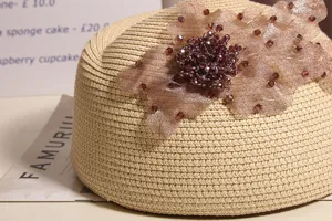 Nahaufnahme der beigen Stroh Beret Mütze Detail mit Strass Mesh Blumen Dekoration.