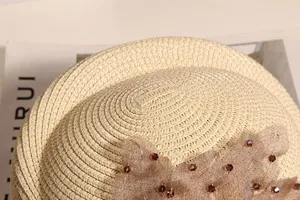 Nahaufnahme der gewebten Strohhutdetails mit zarter Spitzenblume und funkelndem Strass.