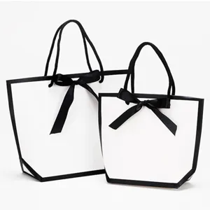 Détail de sac cadeau blanc, bordure noire et nœud papillon, emballage élégant.