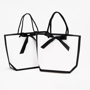 Sacs cadeaux en papier blanc avec bordure noire et beau ruban noir pour emballage.