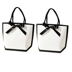 Sac en papier cadeau blanc avec bordure noire et élégant nœud pour le shopping.