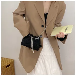 Detail view of a black rhinestone drawstring bucket bag styled with a beige blazer.