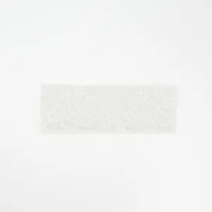 Detail view of a white floral lace headband, showing intricate wavy edge and elastic texture.