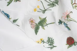 Detail view of white cotton grid fabric embroidered triangular scarf with delicate floral motifs.