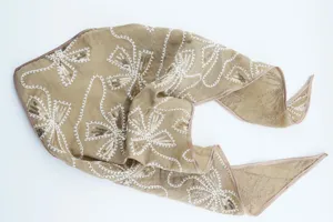 Vista detallada del pañuelo de cabeza bordado con lentejuelas en tono champán y flores.
