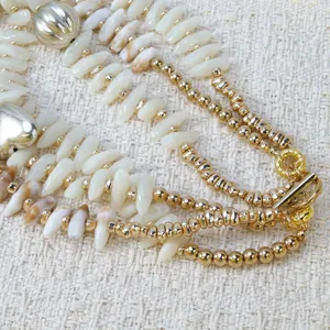 Detalle de collar multicapa con concha y abalorios dorados, joya de playa para mujer.