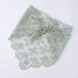 Closeup of sage green lace triangular headscarf featuring floral embroidery and scalloped edges.