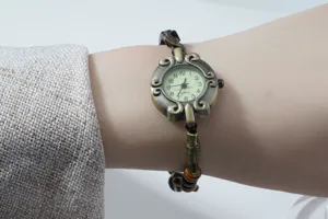 Close-up detail of vintage bronze quartz watch with ornate dial and beaded bracelet strap.