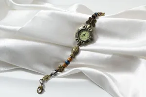 Detail view showing vintage bronze beaded bracelet watch dial, charms, and quartz movement.