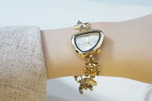 Gold irregular triangular dial quartz watch detail, charm bracelet with cute bear pendant.