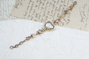 Detail shot of gold charm bracelet watch featuring irregular dial, teddy bear, and star charms.