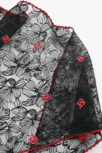 Close-up of black lace triangle scarf with floral embroidery and striking red M logo details.