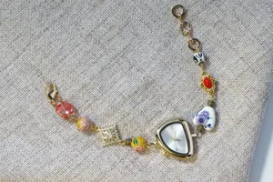 Detailed view of irregular gold watch with beaded ceramic and enamel charm bracelet.