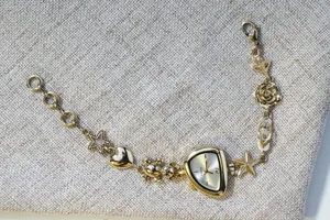 Gold tone charm bracelet watch detail featuring bear, heart, star and rose flower charms.