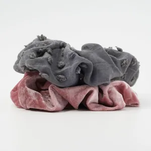 Detailed close-up of stacked fabric scrunchies in grey textured and pink velvet styles.