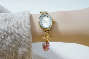 Close-up of elegant oval quartz watch with bee charm, rhinestone markers and beaded bracelet.