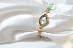 Close-up of luxury oval quartz watch with pearl, floral, and bee charm beaded strap details.