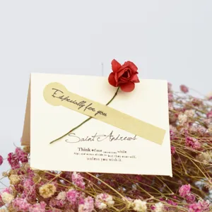 Primer plano detallado de tarjeta de felicitación vintage con flor roja seca y texto.