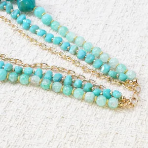 Detailopname van meerstrengse turquoise kralenketting met gouden ketting in boheemse stijl.
