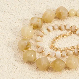 Close-up detail van boheemse meerlagige kralenketting met harsstenen en gouden ketting.